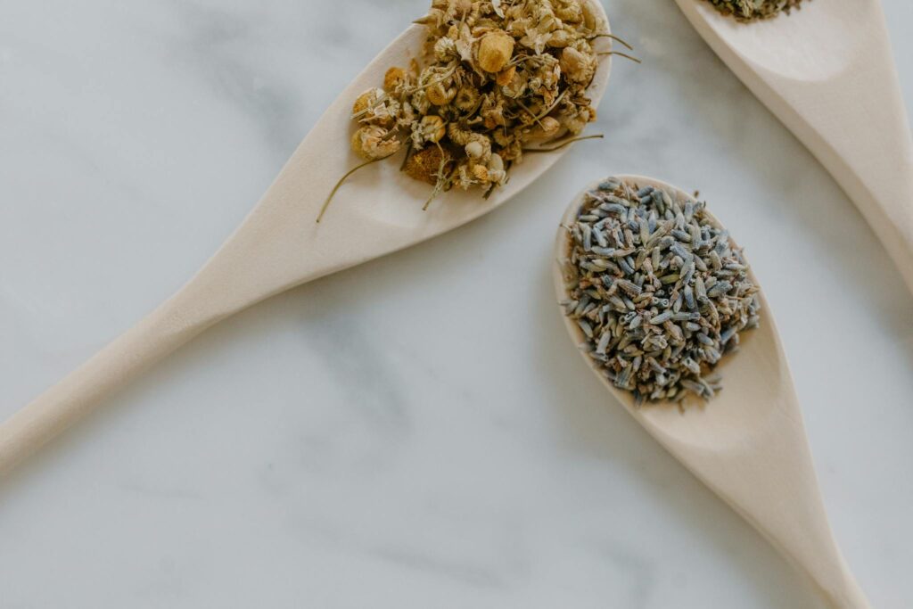 Close-up of chamomile and lavender dried herbs in wooden spoons on white marble.