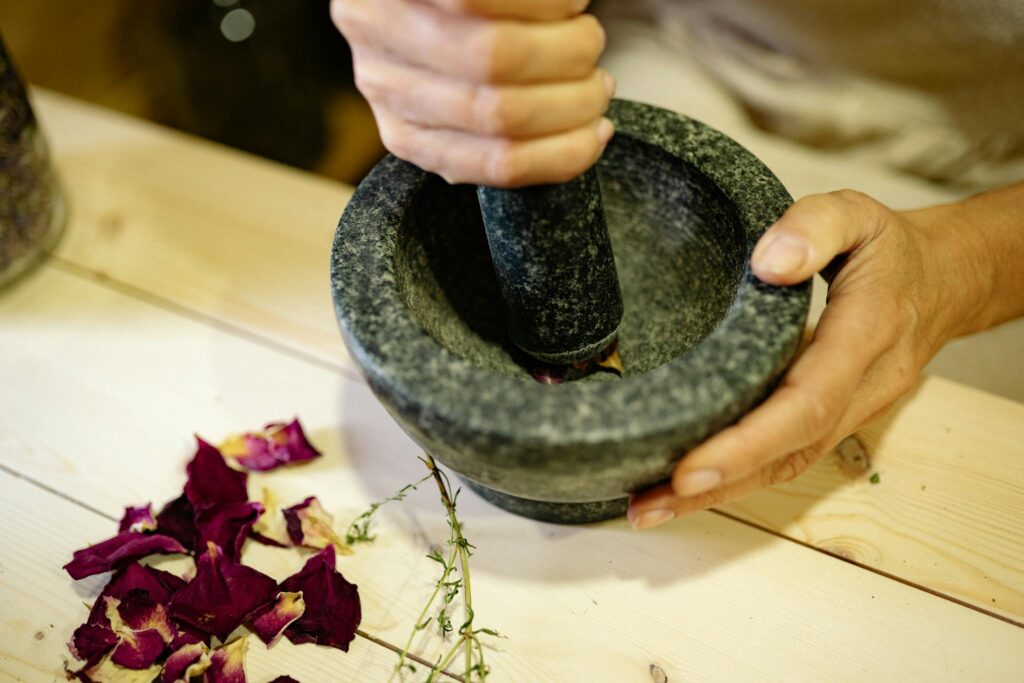 Close-up of hands using a stone mortar and pestle to grind dried rose petals.